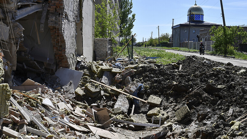 Trümmer liegen in einem flachen Krater einer Explosion neben einem beschädigten Wohnhaus nach russischem Beschuss. Foto: Andriy Andriyenko/AP/dpa