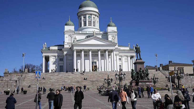 Menschen gehen vor dem Dom von Helsinki unter blauem Himmel im Stadtzentrum. Finnland hat sich wegen des Angriffskriegs des großen Nachbarlandes Russland in der Ukraine auf den Weg in die Nato gemacht. Foto: Martin Meissner/AP/dpa