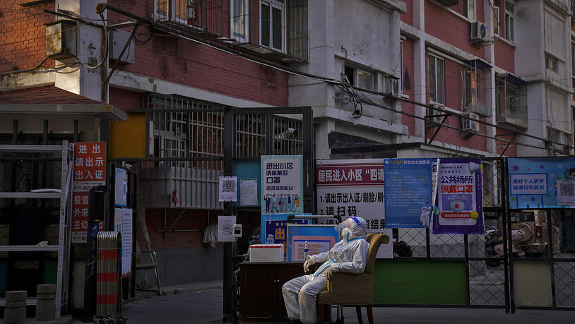 Ein Wachmann im Schutzanzug sitzt an einem Eingangstor zu einem Wohnviertel in Peking. Vor dem Hintergrund steigender Corona-Zahlen haben zwei der größten Städte in China am 21.11.2022 weitere Einschränkungen angekündigt. Foto: Andy Wong/AP/dpa