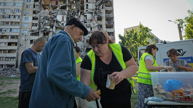 Anwohner erhalten vor dem Hintergrund ihres Wohnhauses, das durch einen russischen Raketenangriff beschädigt wurde, kostenlose Mahlzeiten von Freiwilligen. Foto: Andrii Marienko/AP
