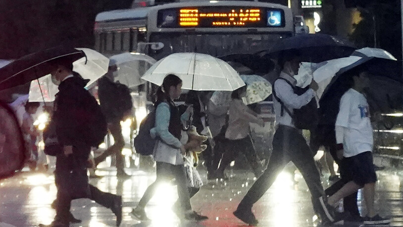 Fußgänger halten Regenschirme gegen starken Wind und Regen, während sie über eine Straße in Kawasaki gehen. Foto: Eugene Hoshiko/AP