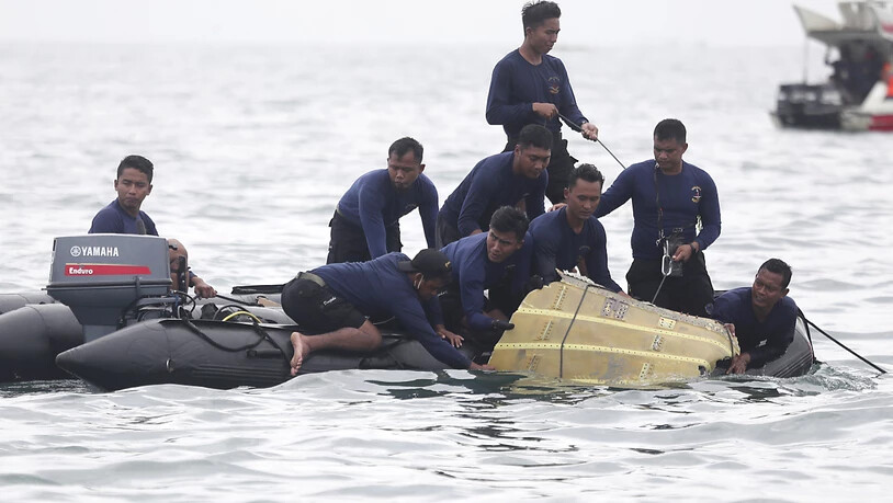 Taucher der indonesischen Marine ziehen ein Flugzeugteil aus dem Wasser. Foto: Achmad Ibrahim/AP/dpa