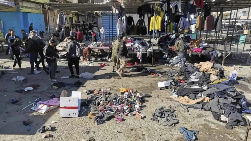 Menschen und Sicherheitskräfte gehen in der irakischen Hauptstadt am Ort eines tödlichen Anschlags, einem Markt, auf dem gebrauchte Kleidung verkauft wurde, an auf dem Boden verstreuten Kleidung und Schuhen vorbei. Foto: Hadi Mizban/AP/dpa