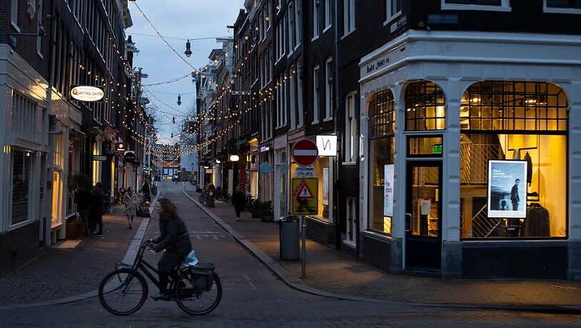 Eine Frau fährt auf ihrem Fahrrad durch das ansonsten fast leere Einkaufsviertel der Neun Straßen in Amsterdam. Foto: Peter Dejong/AP/dpa