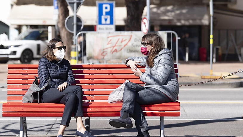 Schutzmasken gehören mittlerweile zum Alltag, so wie hier in Lugano, wo zwei Frauen auf einer Sitzbank verweilen. (Themenbild)
