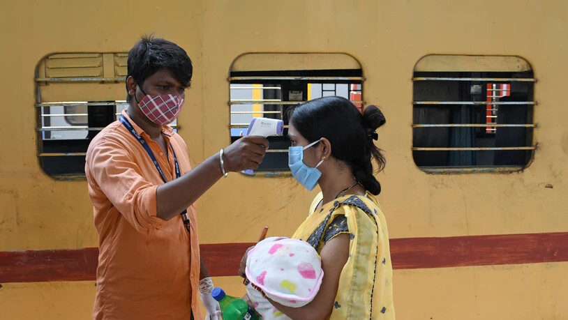 Ein Mitarbeiter misst die Temperatur bei einer Frau, die ein Baby auf dem Arm trägt, auf einem Bahnsteig im indischen Mumbai. Foto: Ashish Vaishnav/SOPA Images via ZUMA Wire/dpa