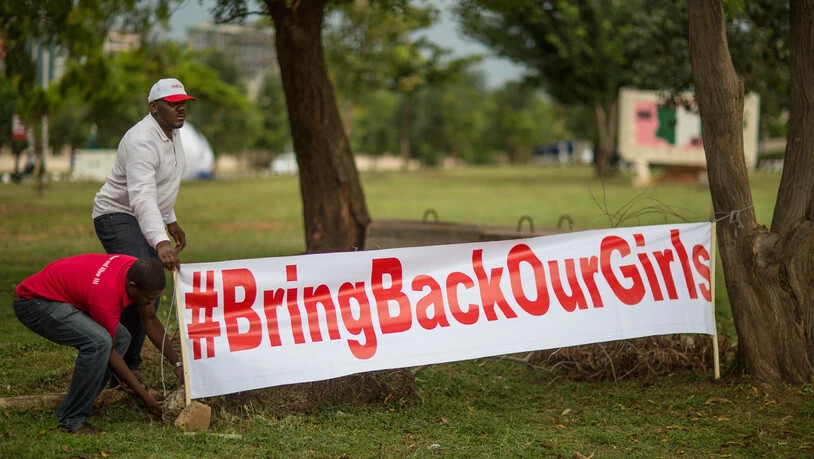 ARCHIV - Aktivisten der Bewegung "Bring back our Girls" (Bringt unsere Mädchen zurück) stellen am 12.06.2014 auf einer Kundgebung in Abuja, Nigeria, ein Transparent mit der Aufschrift "#BringBackOurGirls" auf. Foto: picture alliance / dpa