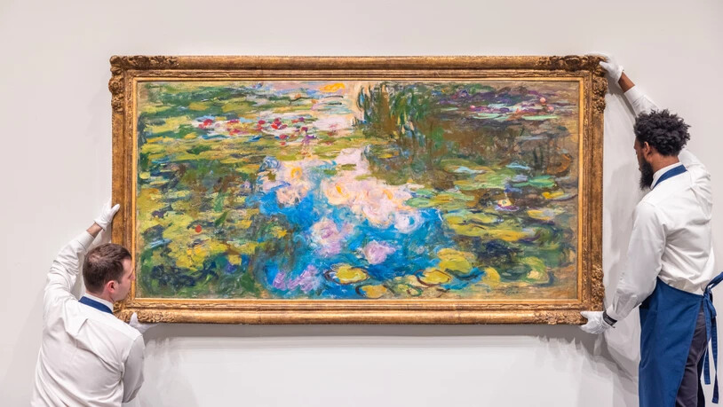 HANDOUT - Mitarbeiter des Auktionshauses Sotheby's hängen ein Seerosen-Werk des französischen Malers Claude Monet (1840-1926) an die Wand. Foto: Sotheby's/PA Media/dpa - ACHTUNG: Nur zur redaktionellen Verwendung im Zusammenhang mit einer…