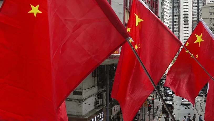 Menschen laufen unter chinesischen Flaggen, die als Teil einer Flaggenzeremonie aufgestellt wurden. Foto: Vincent Yu/AP/dpa
