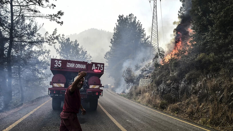 Ein Feuerwehrmann gestikuliert hinter einem Löschzug während am rechten Hang ein Feuer zu sehen ist. Foto: Ismail Coskun/IHA/dpa