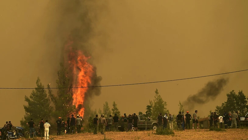 Menschen beobachten die Flammen, die Bäume während eines Waldbrandes im Dorf Avgaria auf der Insel Euböa verbrennen. Der Kampf gegen die Brände im Mittelmeerraum halten weiter an. Besonders dramatisch ist die Lage auf der griechischen Insel Euböa, dort…