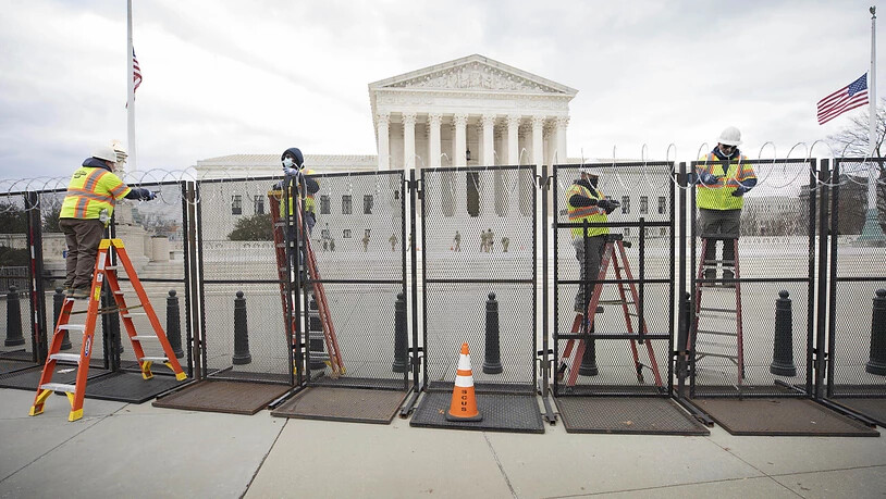 ARCHIV - Arbeiter stehen am Zaun vor dem US-Kapitol während der Sicherheitsvorbereitungen vor der Wiedereröffnung des Gebäudes. Gut acht Monate nach der Erstürmung des Kapitols in Washington bereitet sich die Polizei auf eine weitere Demonstration durch…