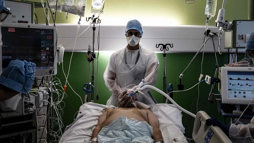 Ein medizinischer Angestellter (M) kümmert sich in der Intensivstation des Krankenhauses Lyon-Süd in Pierre-Benite um einen Corona-Patienten. Foto: Jeff Pachoud/AFP/dpa
