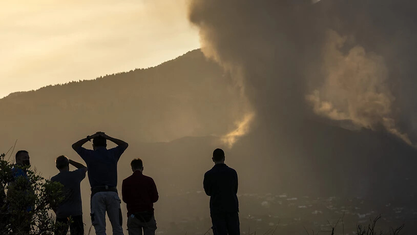 Anwohner blicken von einem Hügel aus auf die Lava, die weiterhin aus einem ausgebrochenen Vulkan auf der Insel La Palma fließt. Foto: Emilio Morenatti/AP/dpa