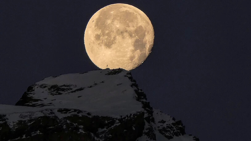 Der untergehende Mond über dem Gipfelkreuz am Calanda.