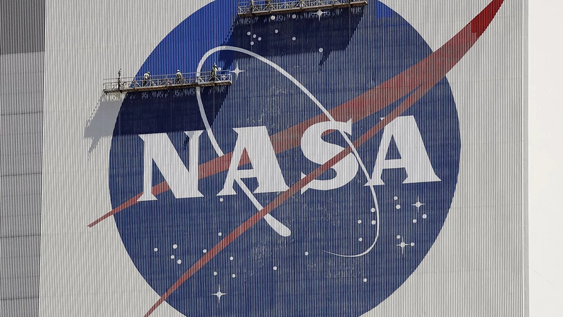 ARCHIV - Arbeiter auf einem Gerüst streichen das NASA-Logo in der Nähe des Fahrzeugmontagegebäudes im Kennedy Space Center. Foto: John Raoux/AP