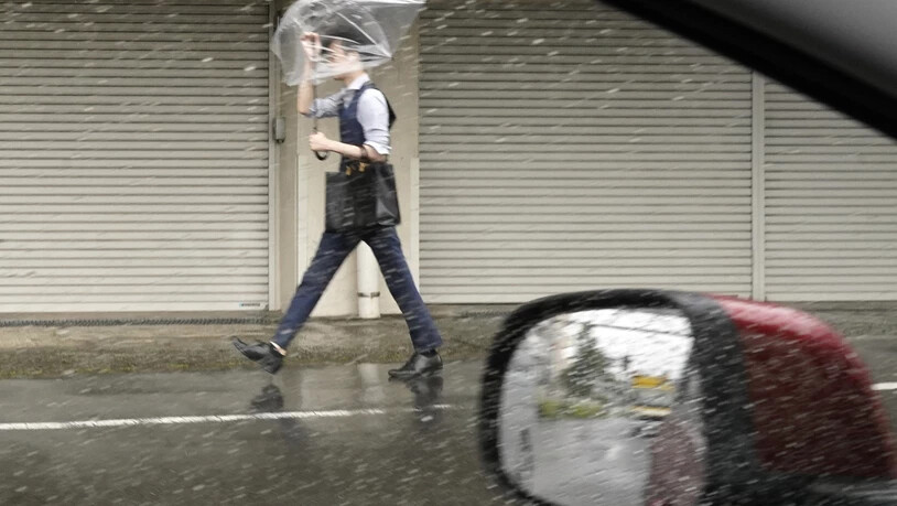 Ein Mann hält einen Regenschirm gegen starken Wind und Regen, während er eine Straße in Tokio entlanggeht. Foto: Eugene Hoshiko/AP/dpa