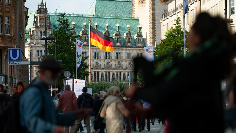 Vor dem Hamburger Rathaus weht eine große Deutschland-Fahne während Besucher über die Ländermeile auf der Mönckebergstraße laufen. Foto: Jonas Walzberg/dpa