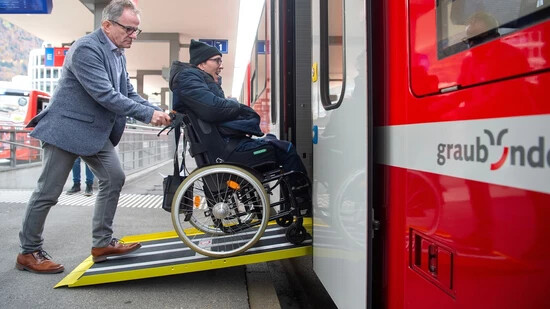 Ersatz- und Übergangsmassnahmen: Philipp Ruckstuhl von Procap Grischun schiebt einen Rollstuhlfahrer über die Rampe in den Zug.
