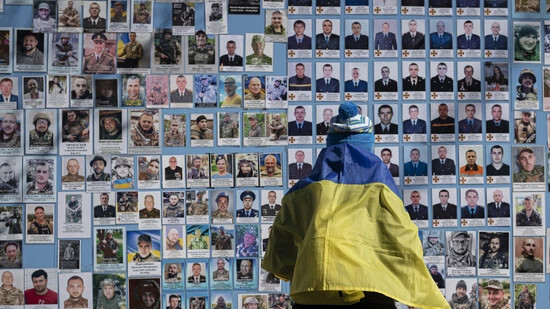 ARCHIV - Eine in eine ukrainische Flagge gehüllte Frau steht neben der Gedenkmauer für die gefallenen Soldaten der Ukraine im russisch-ukrainischen Krieg am ukrainischen Freiwilligentag. Foto: Andrew Kravchenko/AP/dpa