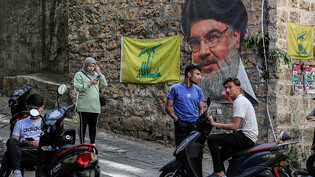 Menschen sitzen in einer Straße mit dem Bild des Hisbollah-Führers Nasrallah und Fahnen, die während der libanesischen Parlamentswahlen 2022 in der Nähe eines Wahllokals in Beirut aufgestellt wurden. Die Libanesen haben inmitten der schwersten…