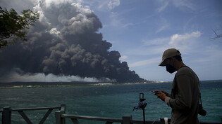 dpatopbilder - Ein Mann tippt auf seinem Handy in der Nähe einer riesigen Rauchwolke, die von einem brennenden Treibstofflager in der Nähe des Hafens von Matanzas aufsteigt, während Feuerwehrleute daran arbeiten, den Brand zu löschen. Fast drei Tage nach…