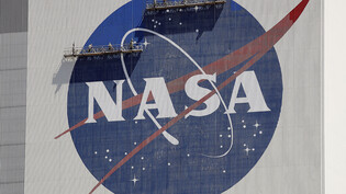 ARCHIV - Arbeiter auf einem Gerüst streichen das NASA-Logo in der Nähe des Fahrzeugmontagegebäudes im Kennedy Space Center. Foto: John Raoux/AP