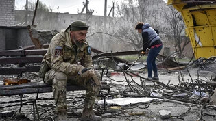 Ein ukrainischer Soldat raucht, während ein Anwohner Trümmer in der Region Saporischschja aufräumt. Durch russische Raketentreffer wurden hier kürzlich mindestens vier Menschen getötet. Foto: Andriy Andriyenko/AP/dpa